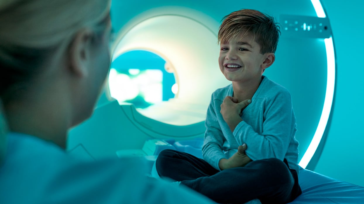 A smiling boy sitting on the table of a medical scanner