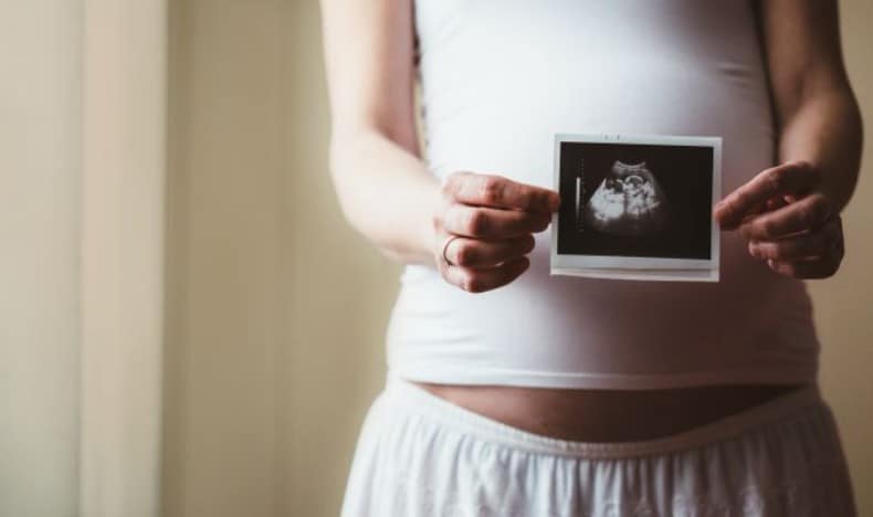 A pregnant person holds up a printed ultrasound image over her belly.