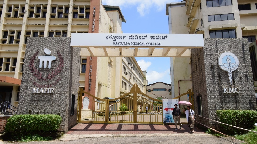 The entrance of Kasturba Medical College Manipal, with people walking in and out of the facility premises