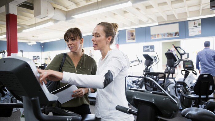 Saleswoman helping woman browsing cardio machines at home gym equipment store