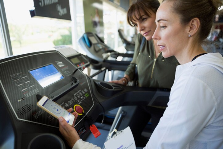 Saleswoman with smart phone fitness tracker on treadmill in home gym equipment store