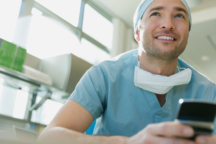 Mid adult male surgeon with mobile phone looking away in clinic