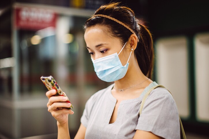 Young lady in mask using smartphone on platform
