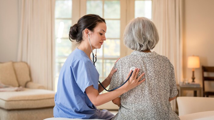 Nurse listening to chest of patient in home