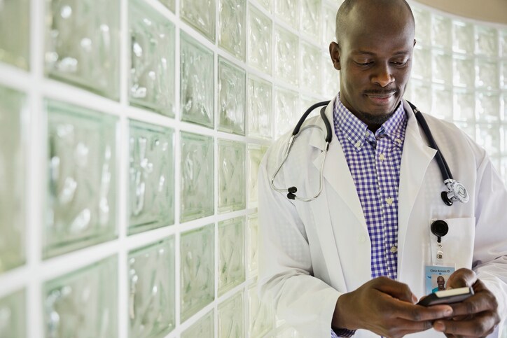 Mid adult male doctor text messaging while standing in hallway